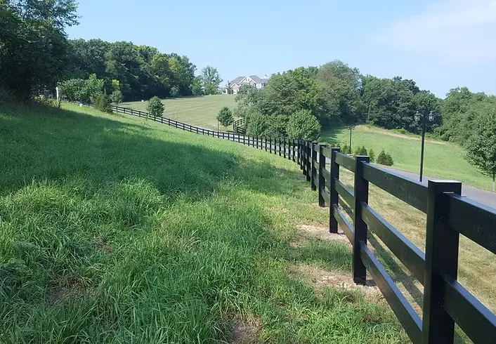 Black vinyl horse rail fence following a green hillside
