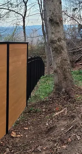 Stained wood fence panels with black framing fitted along a wooded hillside