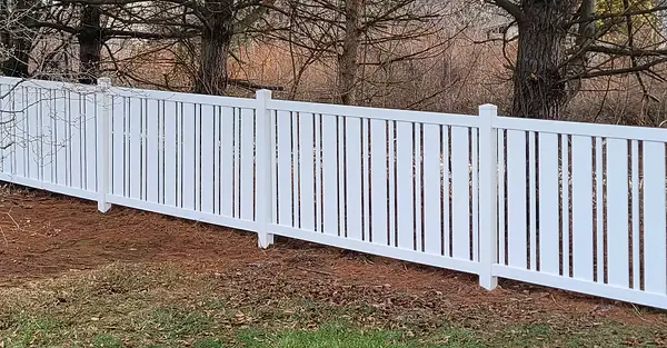 White vinyl picket fence following a wooded residential property line