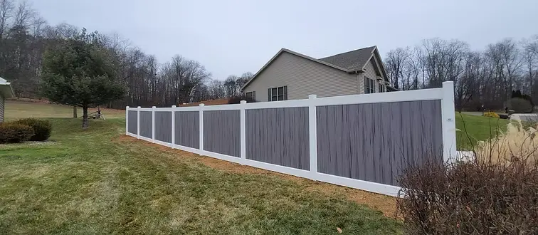 Gray vinyl privacy fence with white posts and rails across a backyard