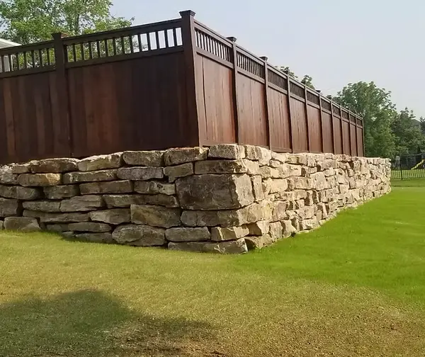 Dark stained wood privacy fence built above a natural stone retaining wall