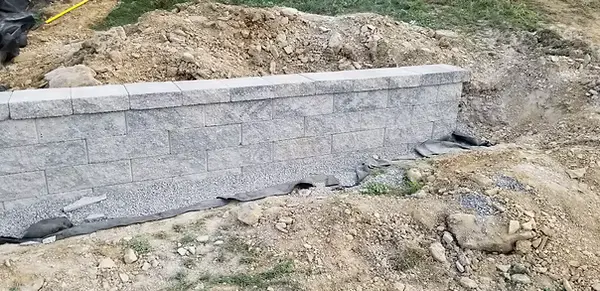 Straight gray block retaining wall built into a sloped yard