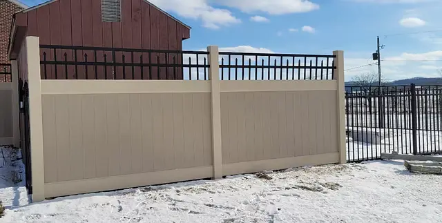 Tan vinyl privacy fence with a dark decorative accent beside an aluminum gate