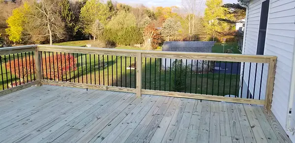 Wood deck with black baluster railings beside a white home